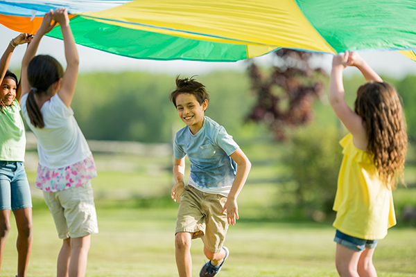 Groupe d'enfants souriants jouant avec un parachute coloré dans un parc par une journée ensoleillée