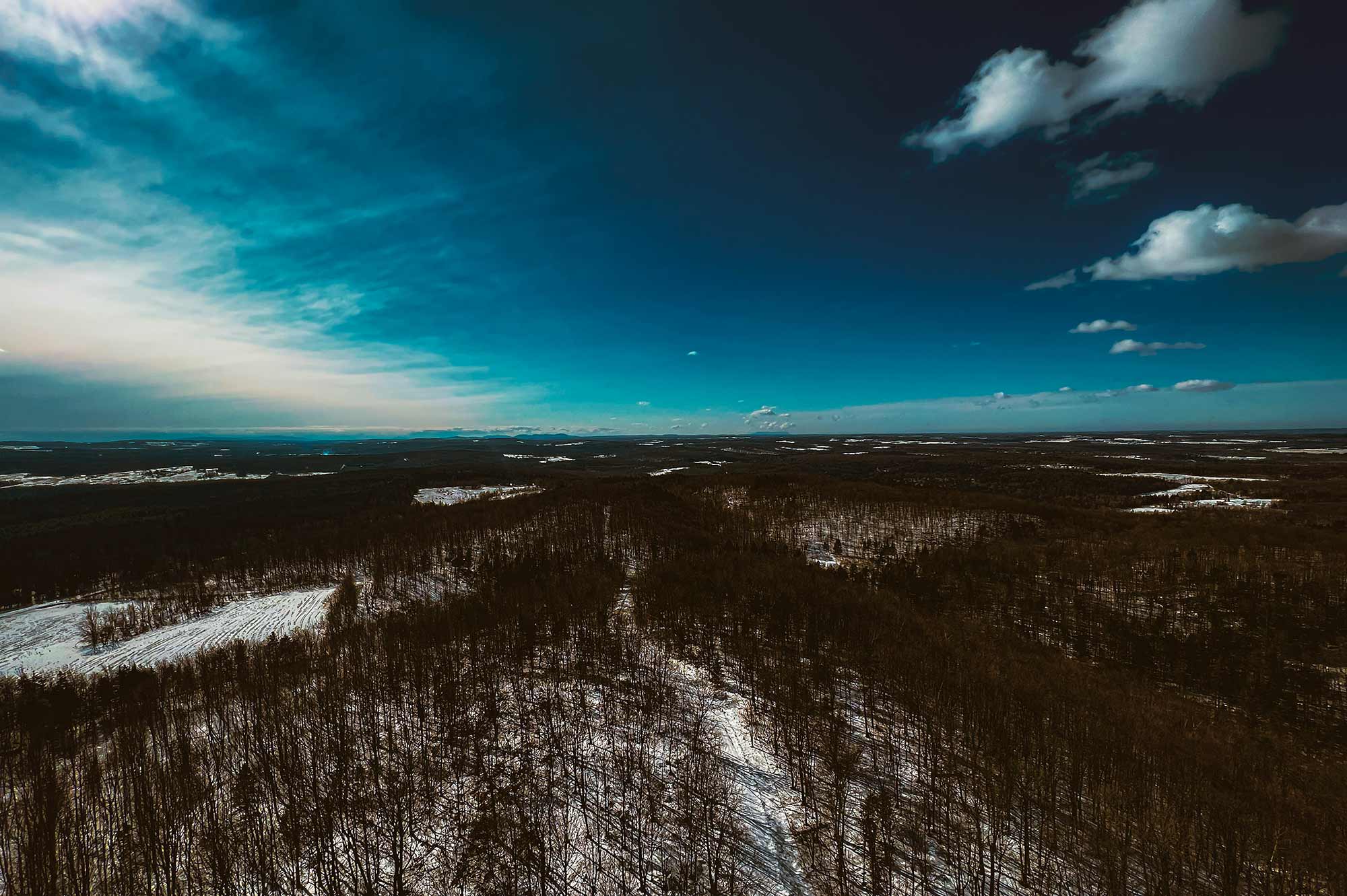 Vue aérienne d’un paysage hivernal avec forêt enneigée sous un ciel bleu dégagé