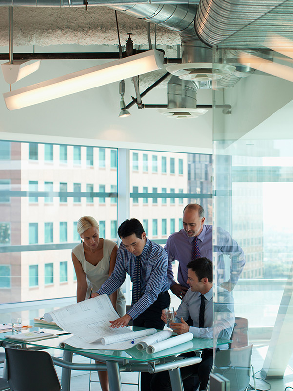 Équipe de professionnels analysant des plans techniques autour d'une table dans un bureau moderne