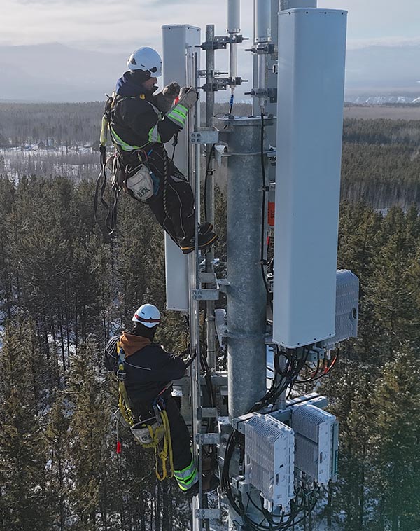 Deux techniciens avec harnais de sécurité installant des antennes sur une tour de télécommunication en hiver