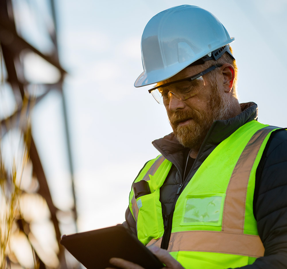 Travailleur de la construction avec casque et veste haute visibilité consultant une tablette sur un chantier